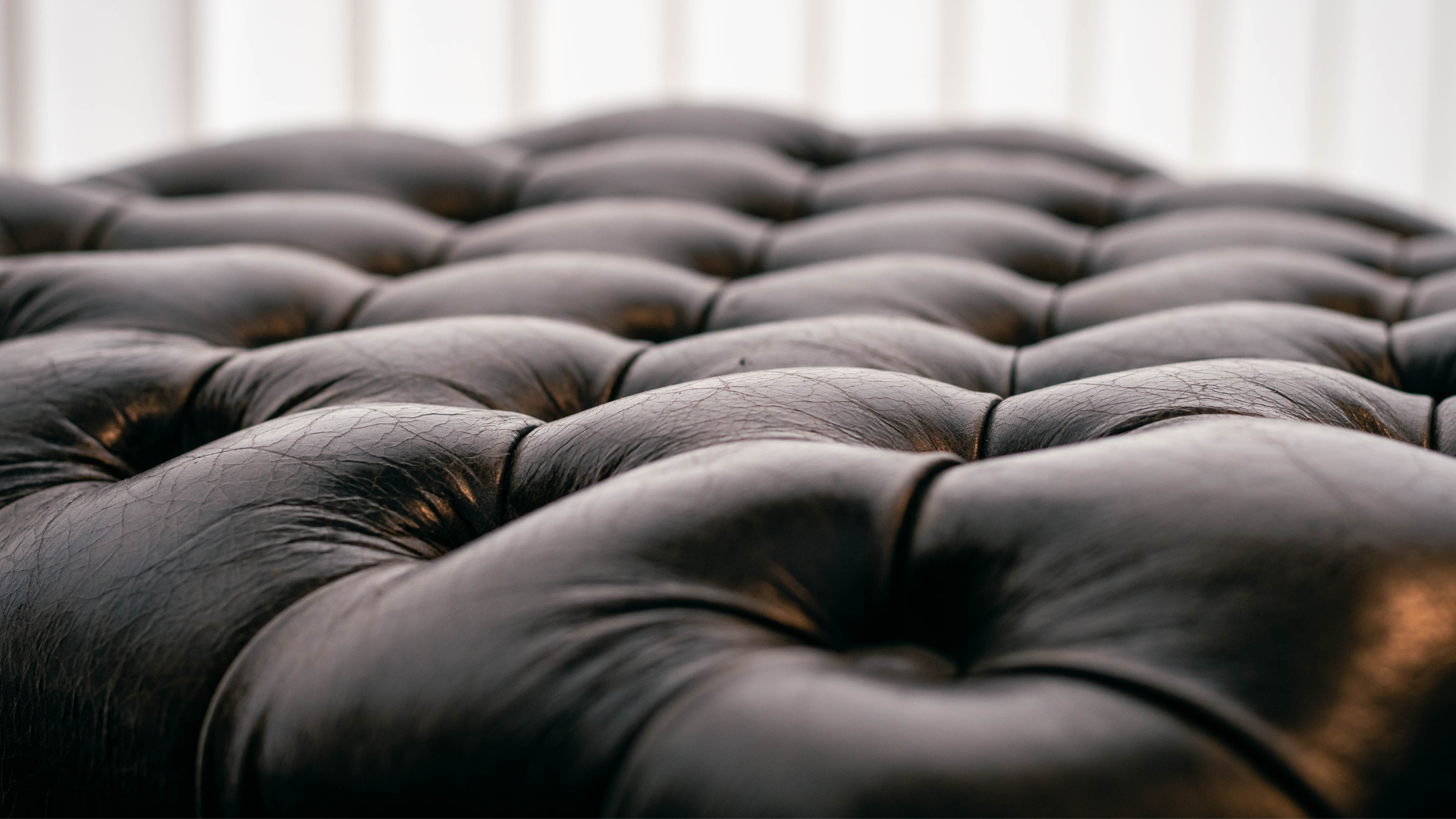 A close up of a black tufted leather ottoman.