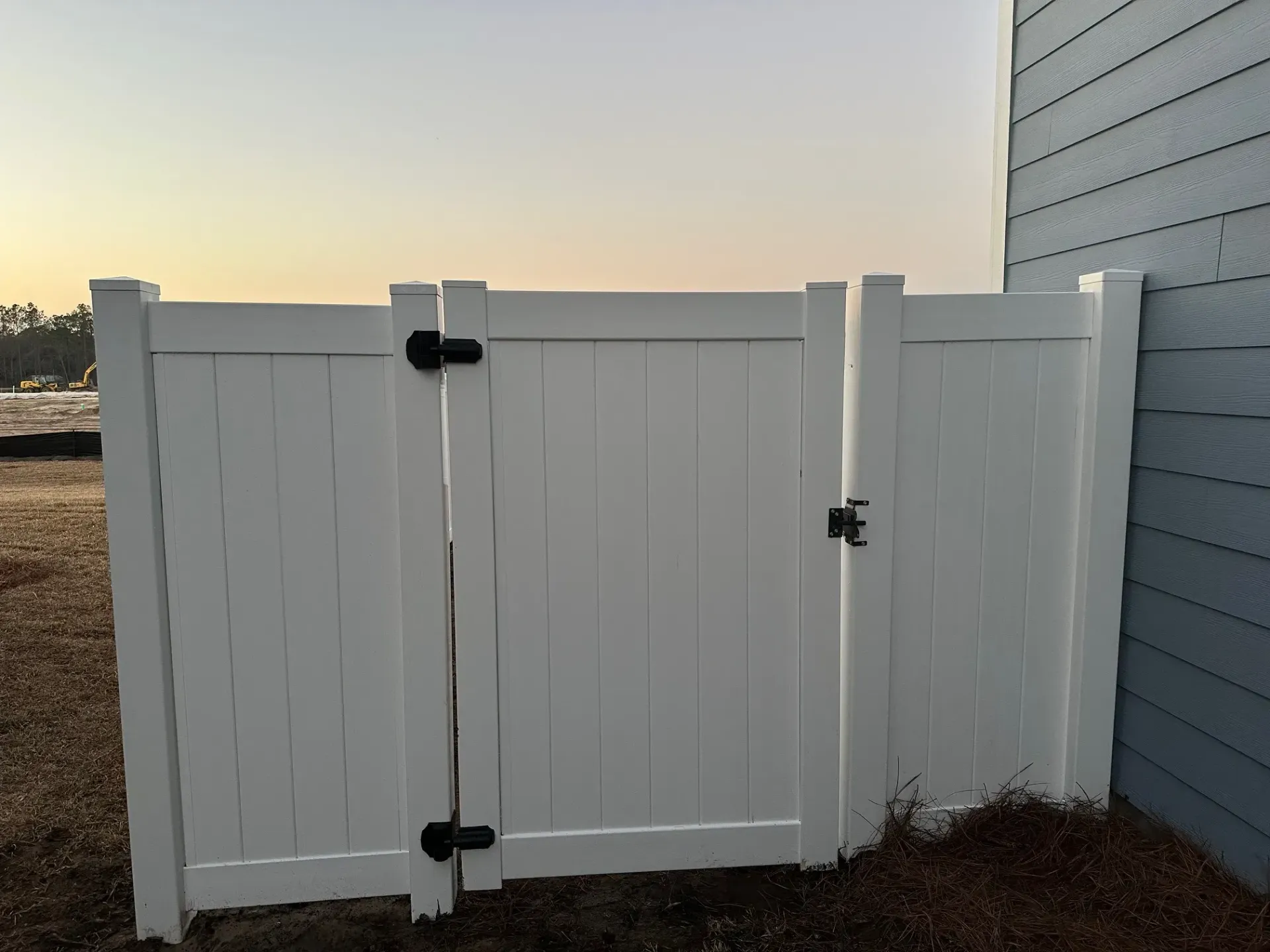 White vinyl fence with two gates, black hardware, next to a blue house.
