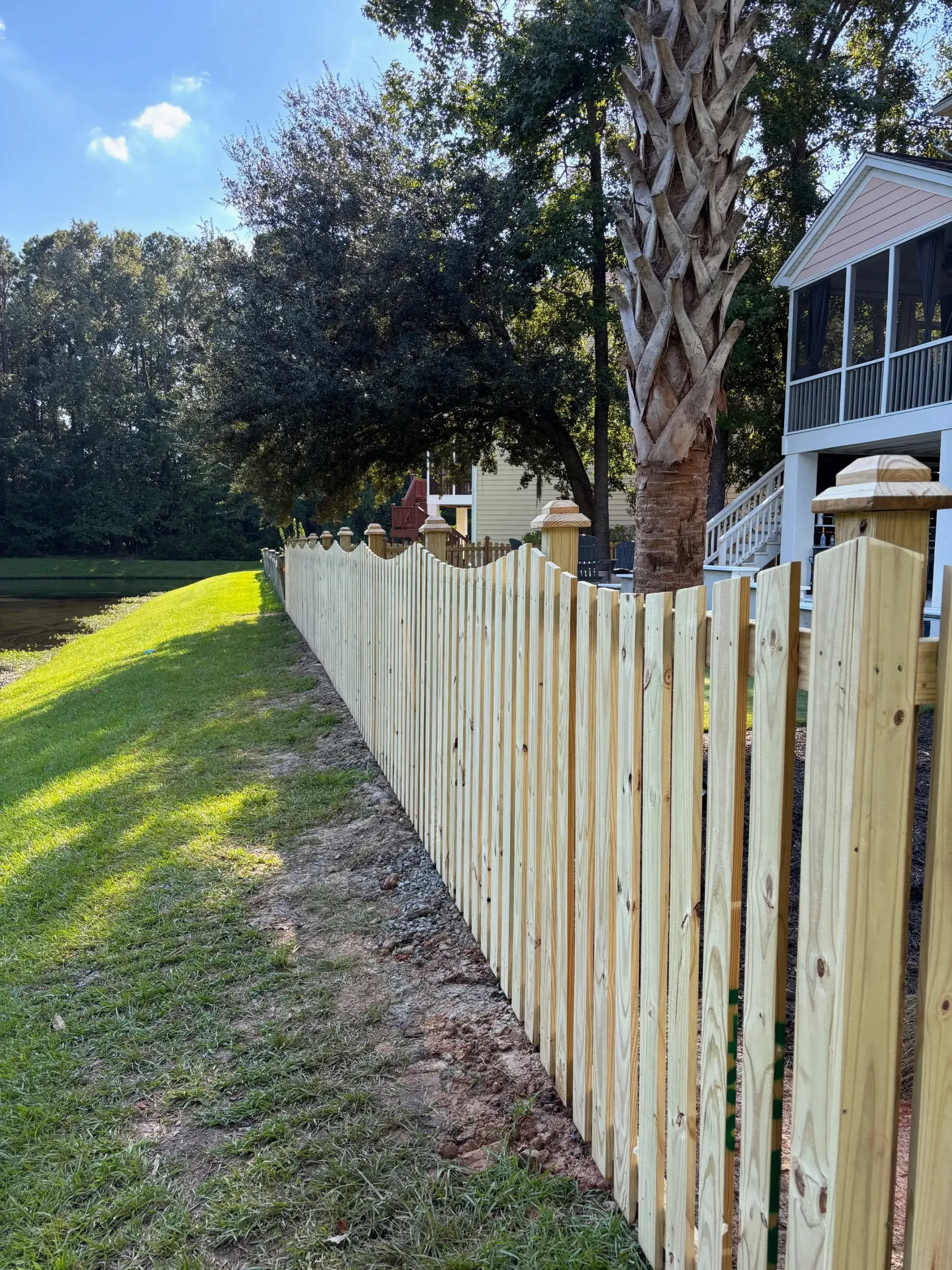 Wooden fence bordering a grassy yard, leading towards a house with a screened porch.