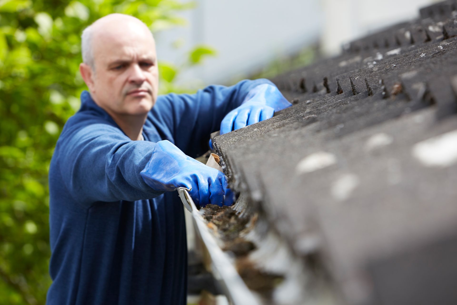 Worker in blue gloves cleaning debris from a dark industrial conveyor belt outdoors