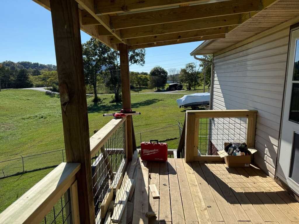 Deck under construction with tool bag, overlooking a grassy field.