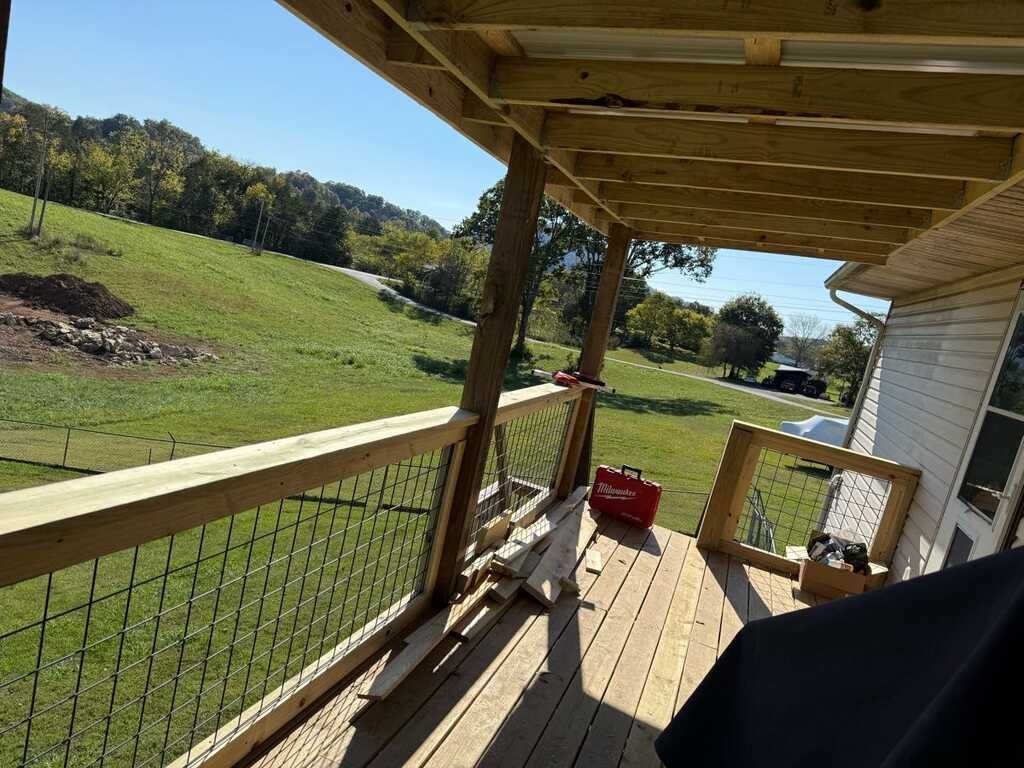 Wooden deck with railing overlooking a grassy hillside, sunny day.