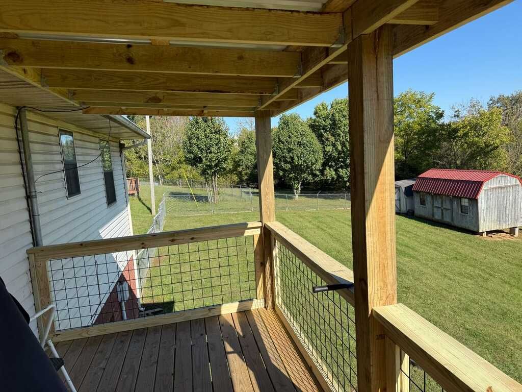 Wooden porch overlooking a grassy yard. Shed in the background, clear blue sky.