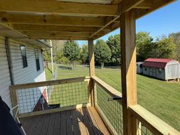 Wooden deck overlooking a grassy yard. Shed and trees in the distance. Blue sky.