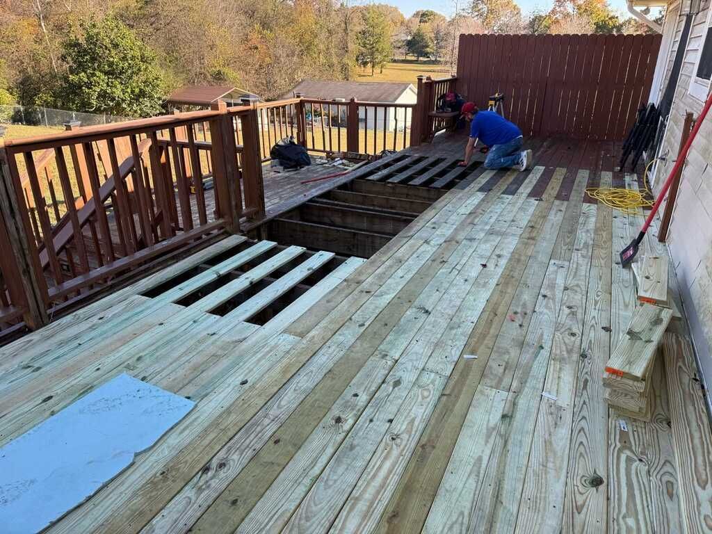 Deck under construction; worker installing wooden planks. Sunlight, fall foliage in background.