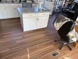 Kitchen with white cabinets, island with granite countertop, and wood-look flooring. A chair with a blanket sits nearby.