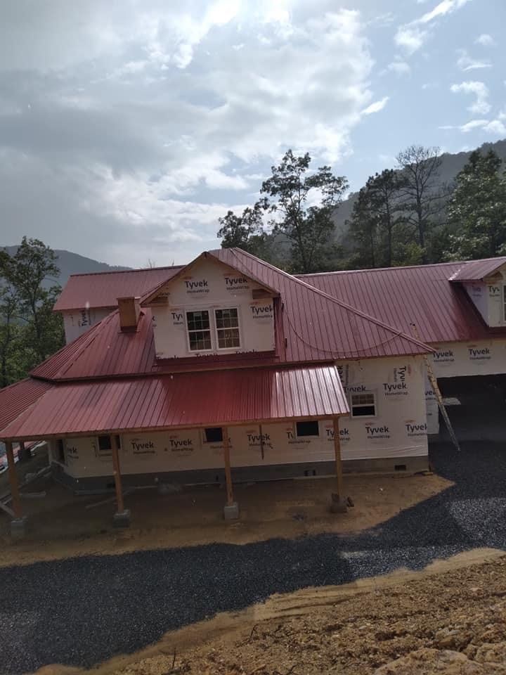 New house under construction with a red metal roof against a mountain backdrop.