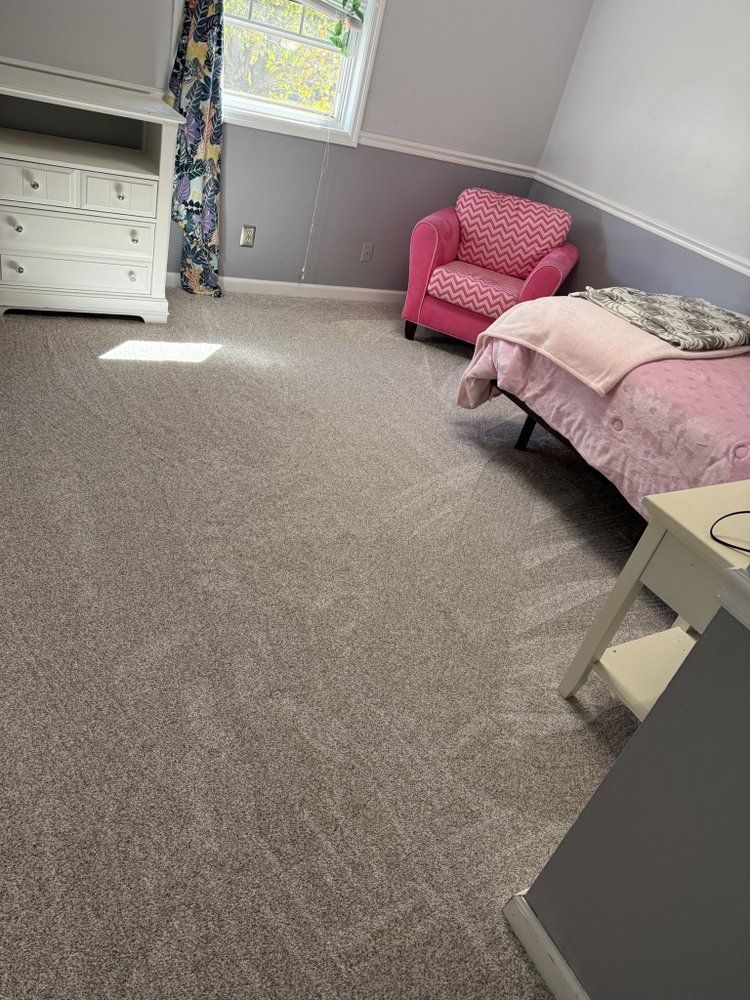 A bedroom with a bed, dresser, pink chair, and gray carpet.