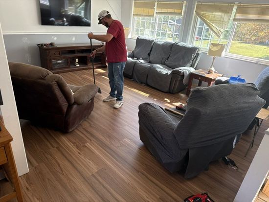 Man in red shirt working on a living room floor with wood-look laminate.