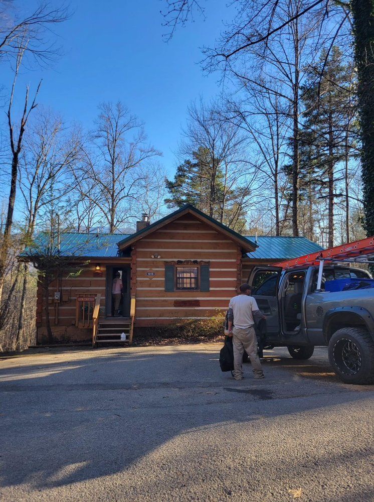Log cabin with a truck parked in front; person exiting truck carrying a bag.