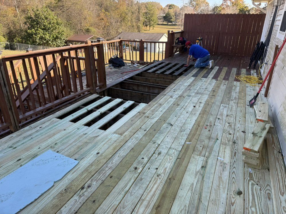 Deck under construction with visible support beams, a person working on the deck, and a brown fence.