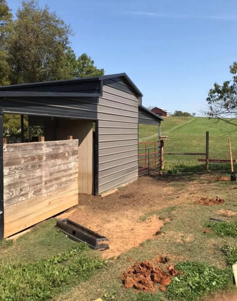 A gray metal barn with a wooden opening, set in a grassy field on a sunny day.