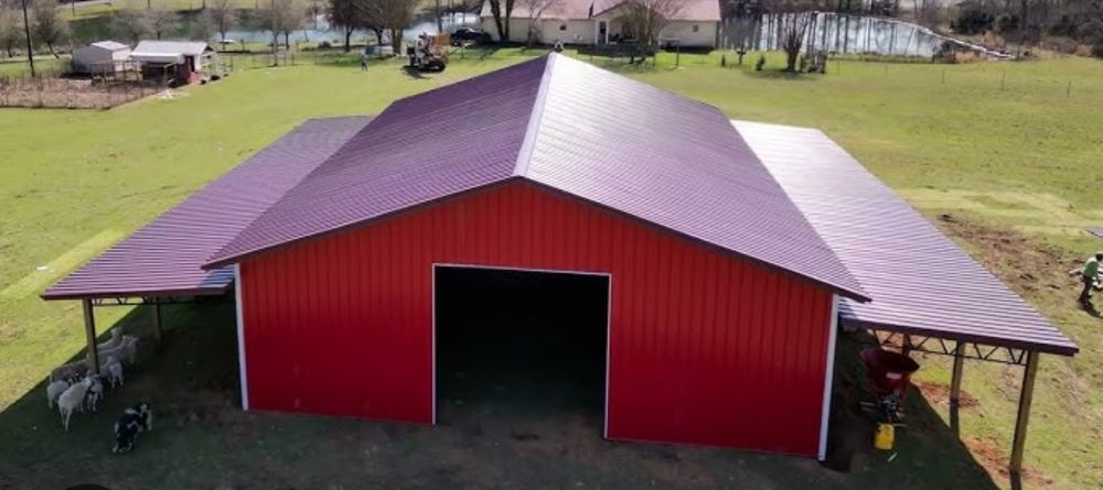Red barn with open doorway, flanked by covered areas, in a grassy field.