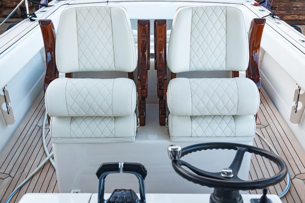 A boat cockpit featuring two white, diamond-stitched swivel seats, a steering wheel, and throttle controls on a teak deck.