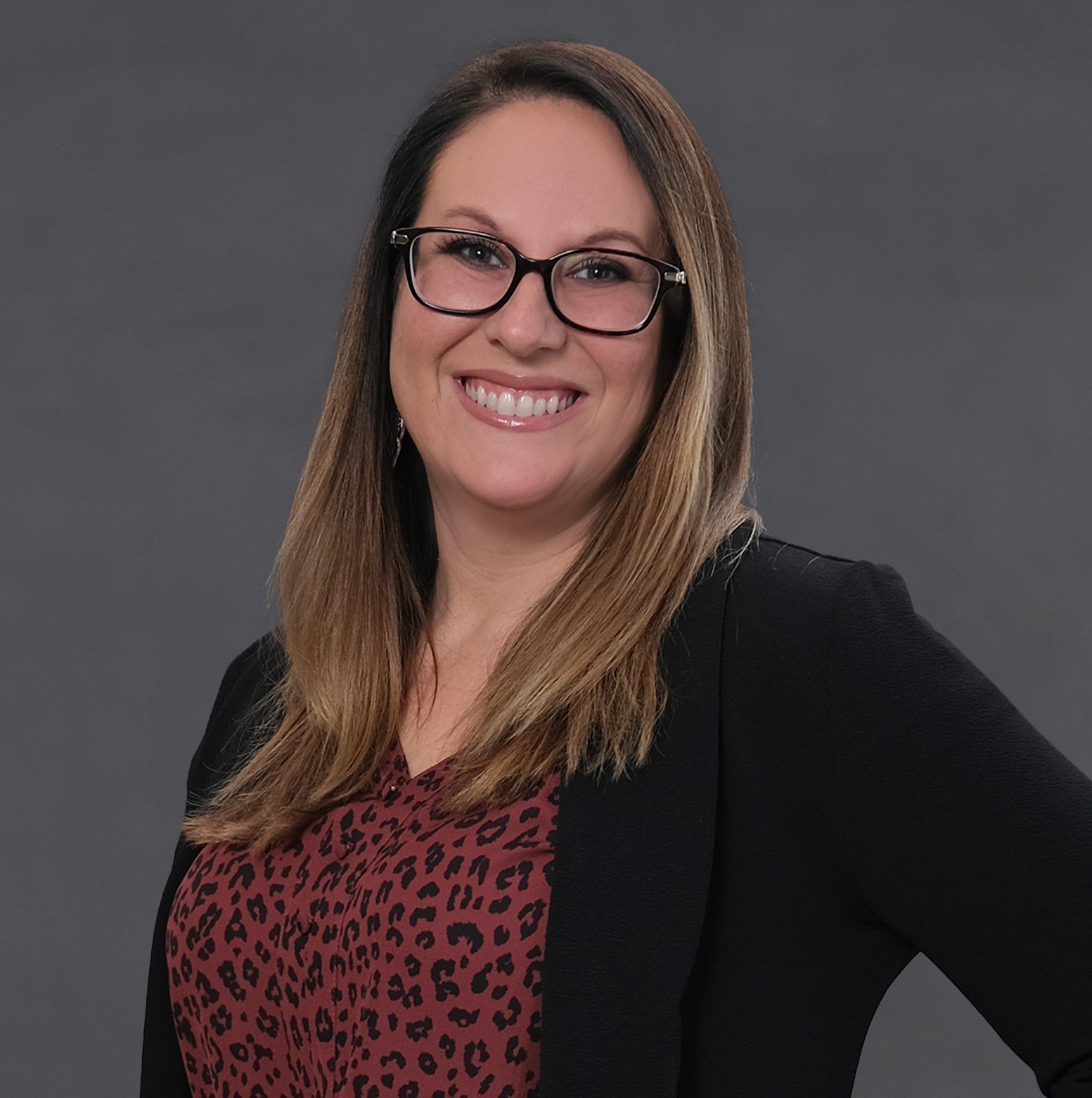 A woman wearing glasses and a black jacket is smiling for the camera.
