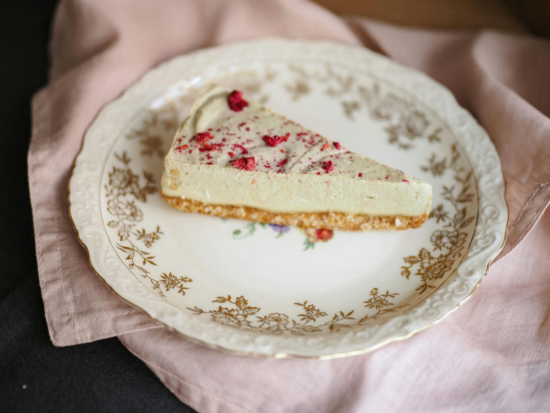 Slice of white cheesecake with red sprinkles on a vintage floral plate, on a pink cloth.