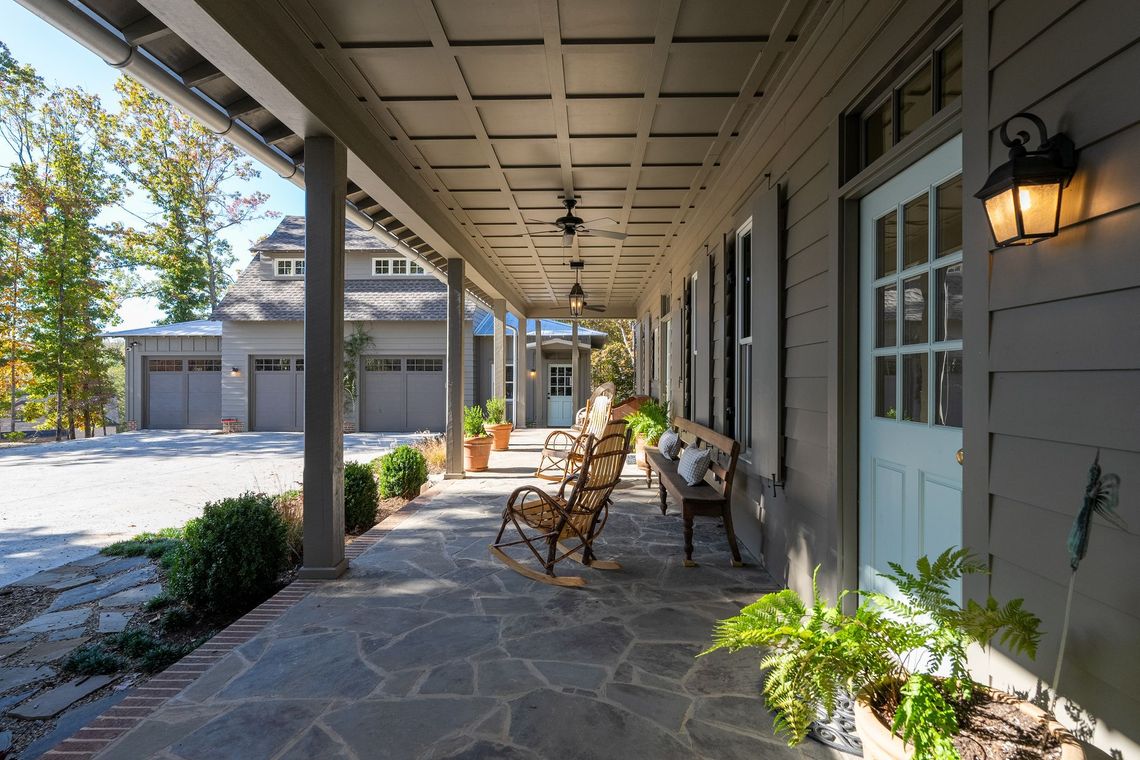 A porch with rocking chairs and a bench in front of a house.