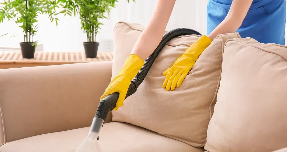 A woman is cleaning a couch with a vacuum cleaner.