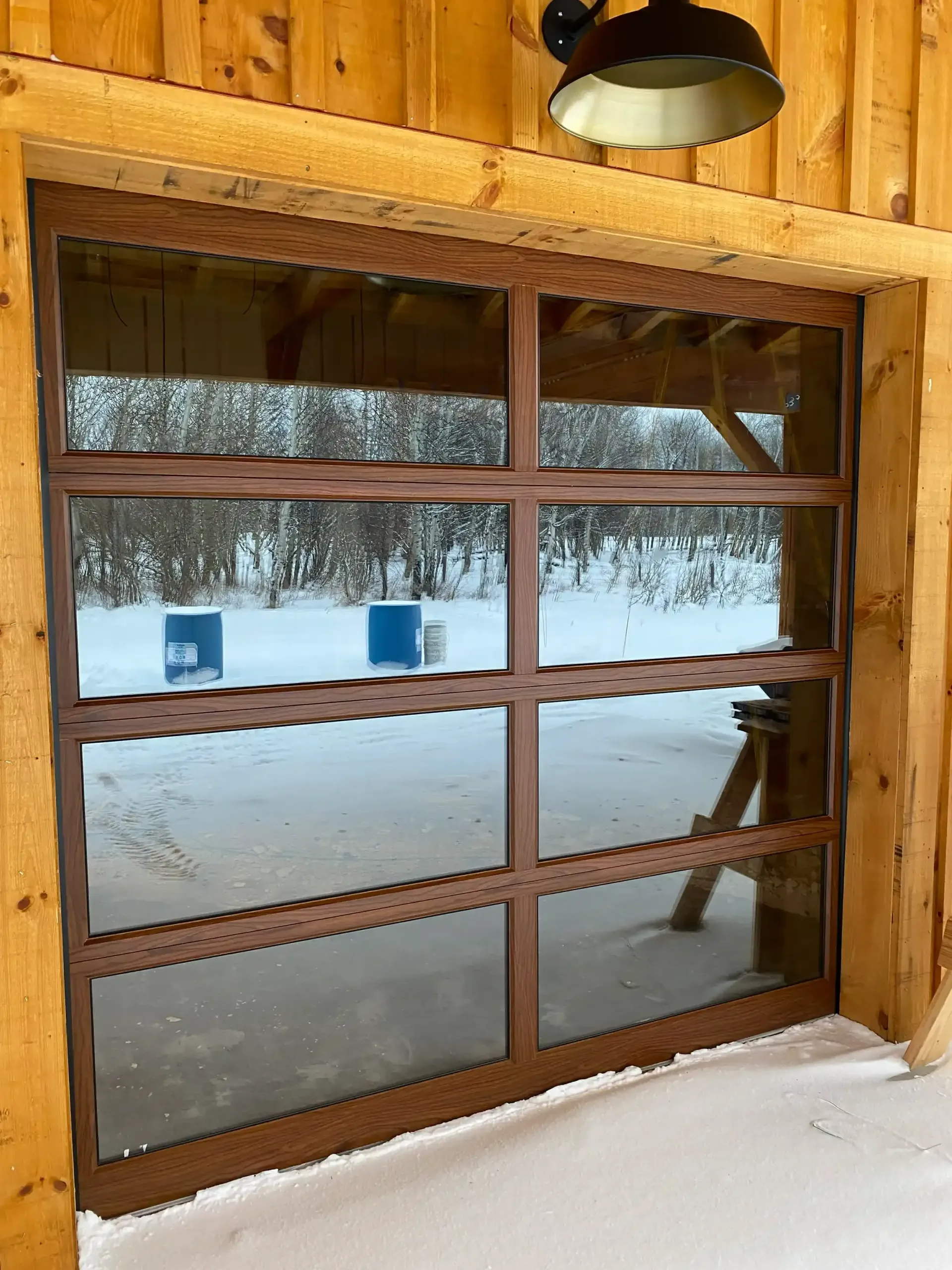 A wooden garage door is open to a snowy yard.
