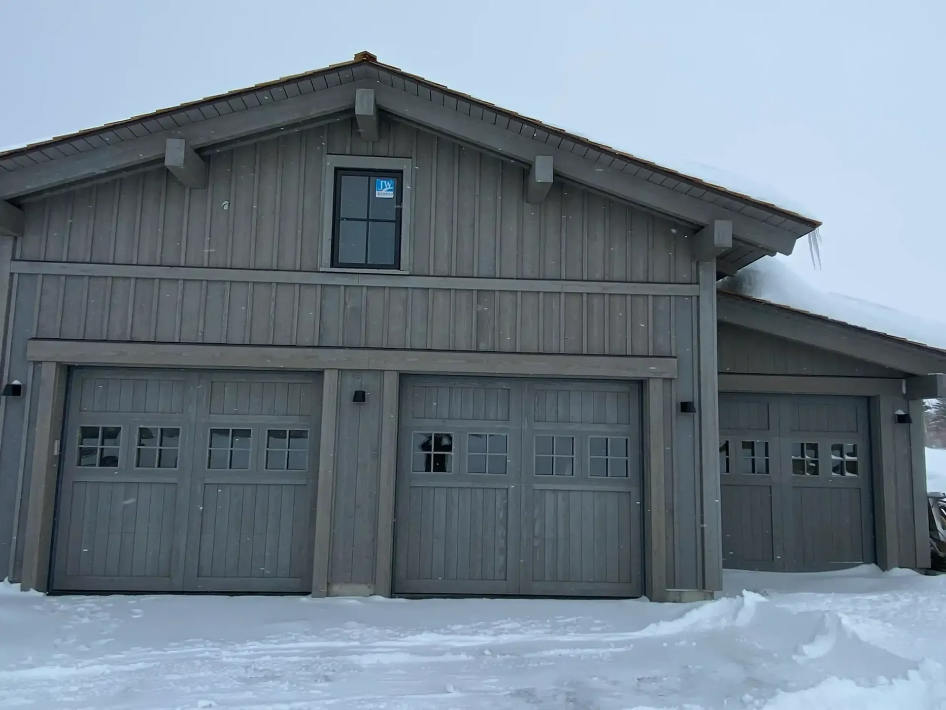 A house with three garage doors is covered in snow