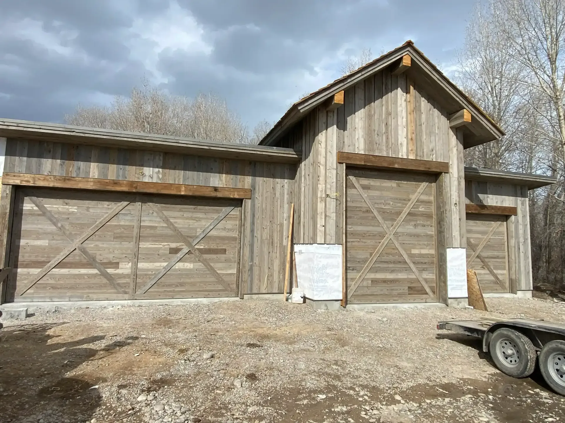 A wooden garage with a trailer parked in front of it.