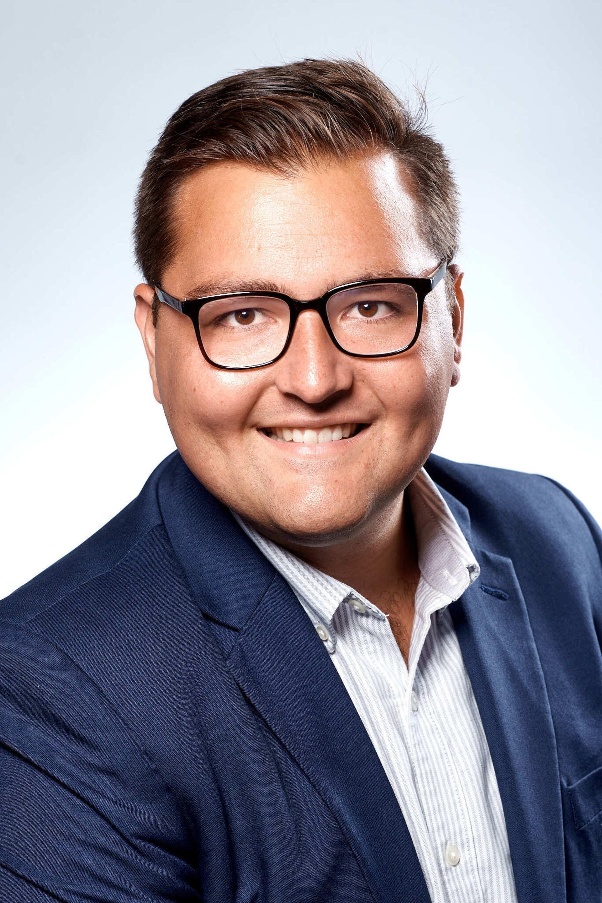 Man wearing glasses, blazer, smiling.