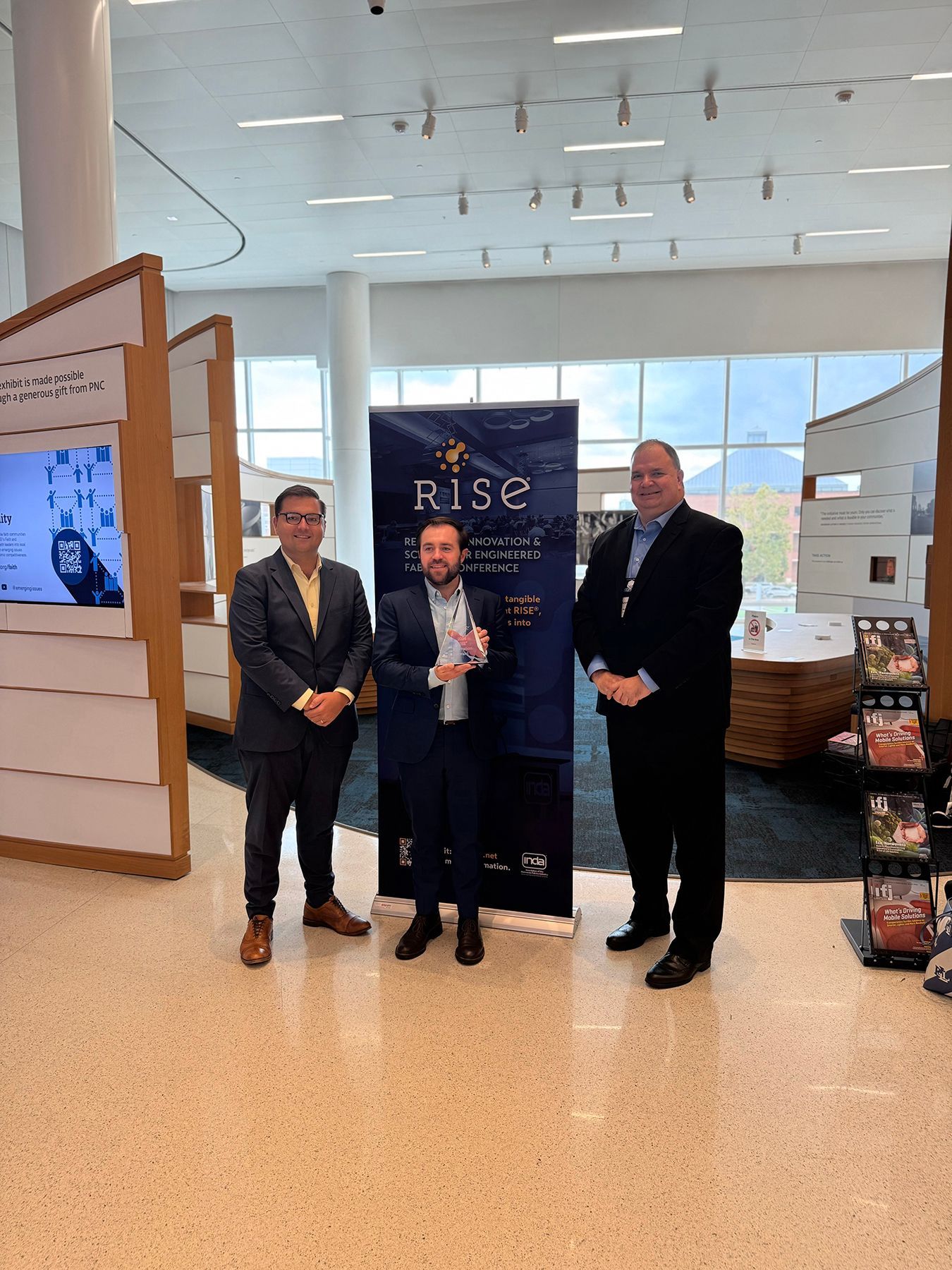 Three men standing with an award and banner that reads 