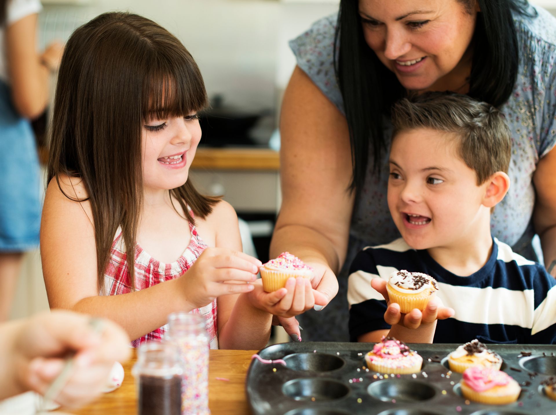 Woman and children decorating cupcakes together in kitchen.