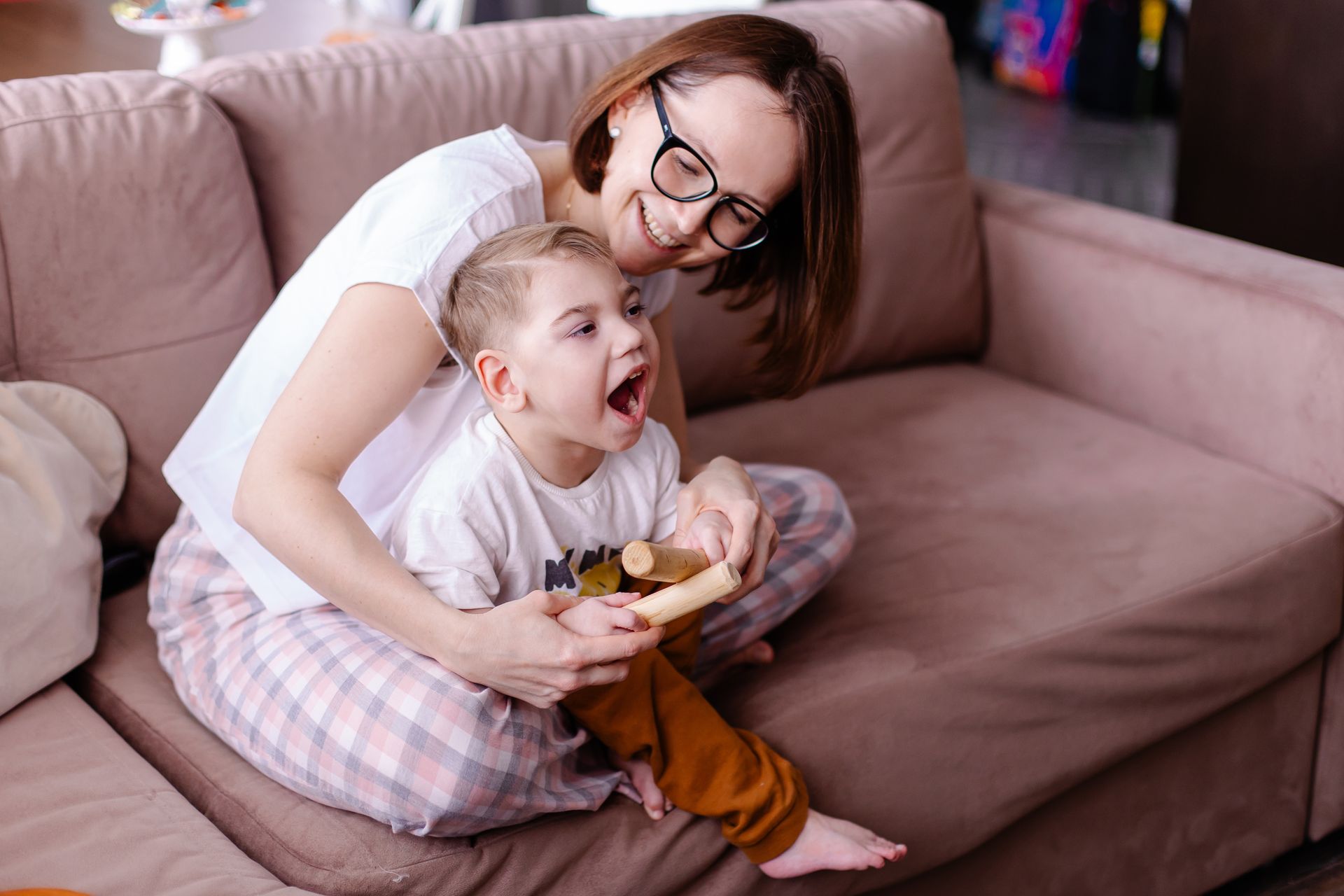 Woman and child on couch, smiling. Child opens mouth wide. Beige couch in home setting.