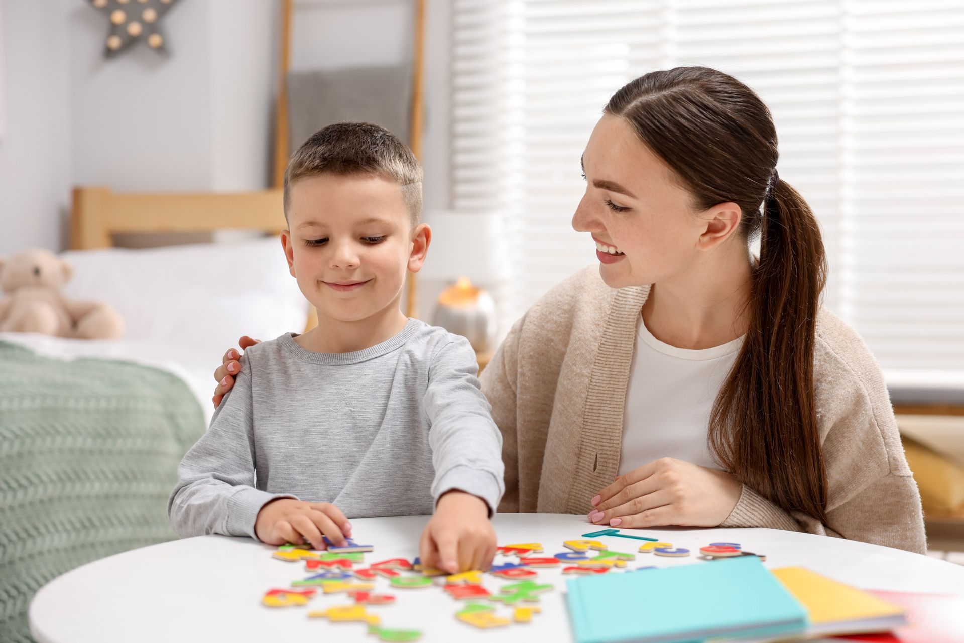 Woman helping a child assemble a colorful puzzle at a round table, indoors.