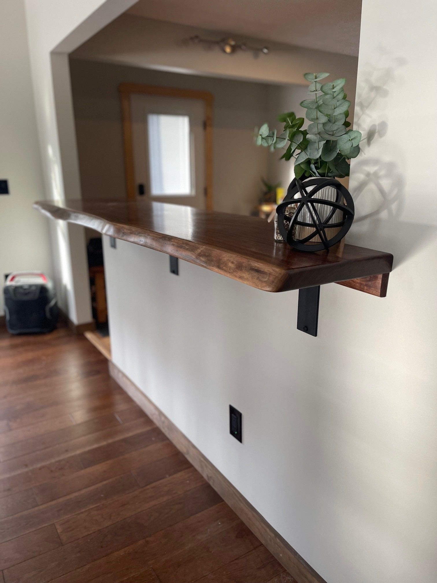 A wooden shelf with a vase of flowers on top of it in a living room.