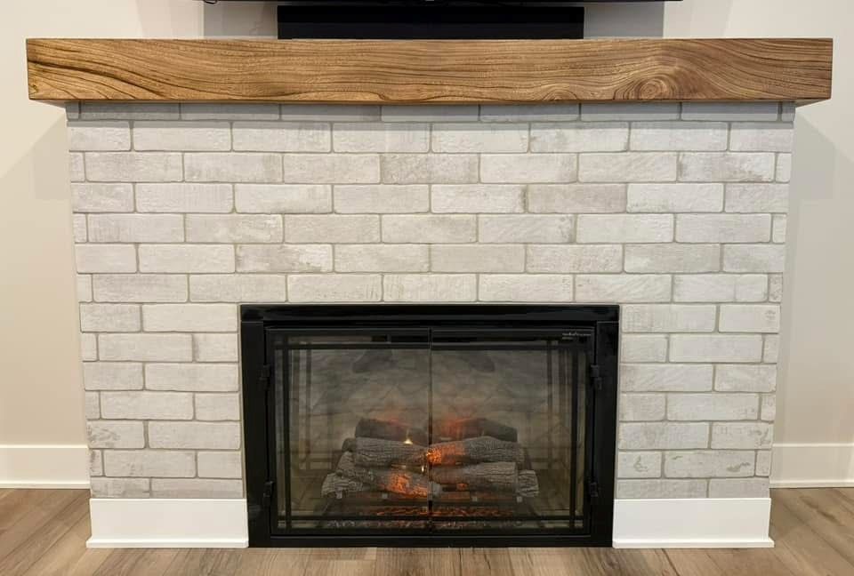 A white brick fireplace with a wooden mantle in a living room.