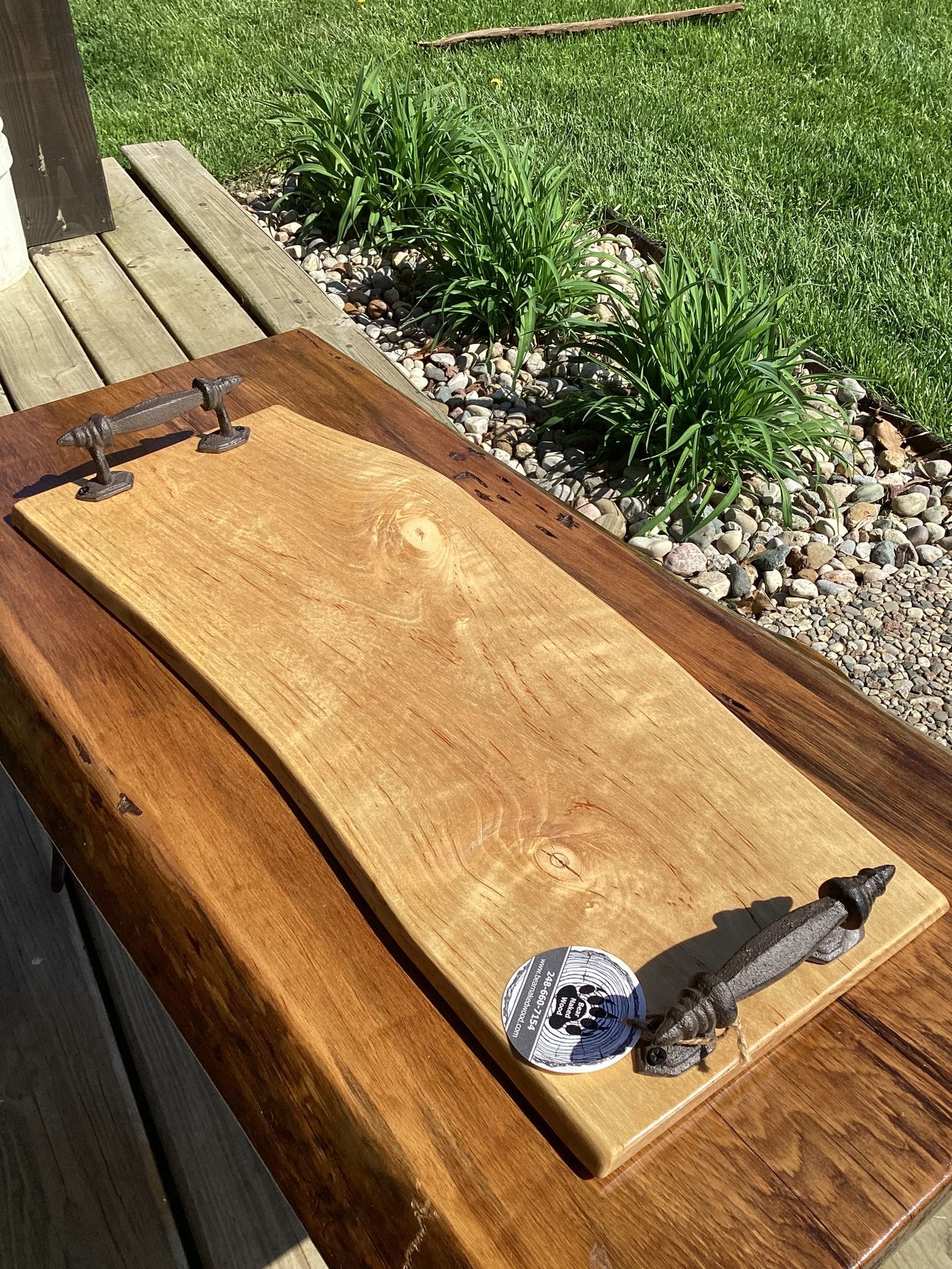 A wooden cutting board with metal handles is sitting on a wooden table.