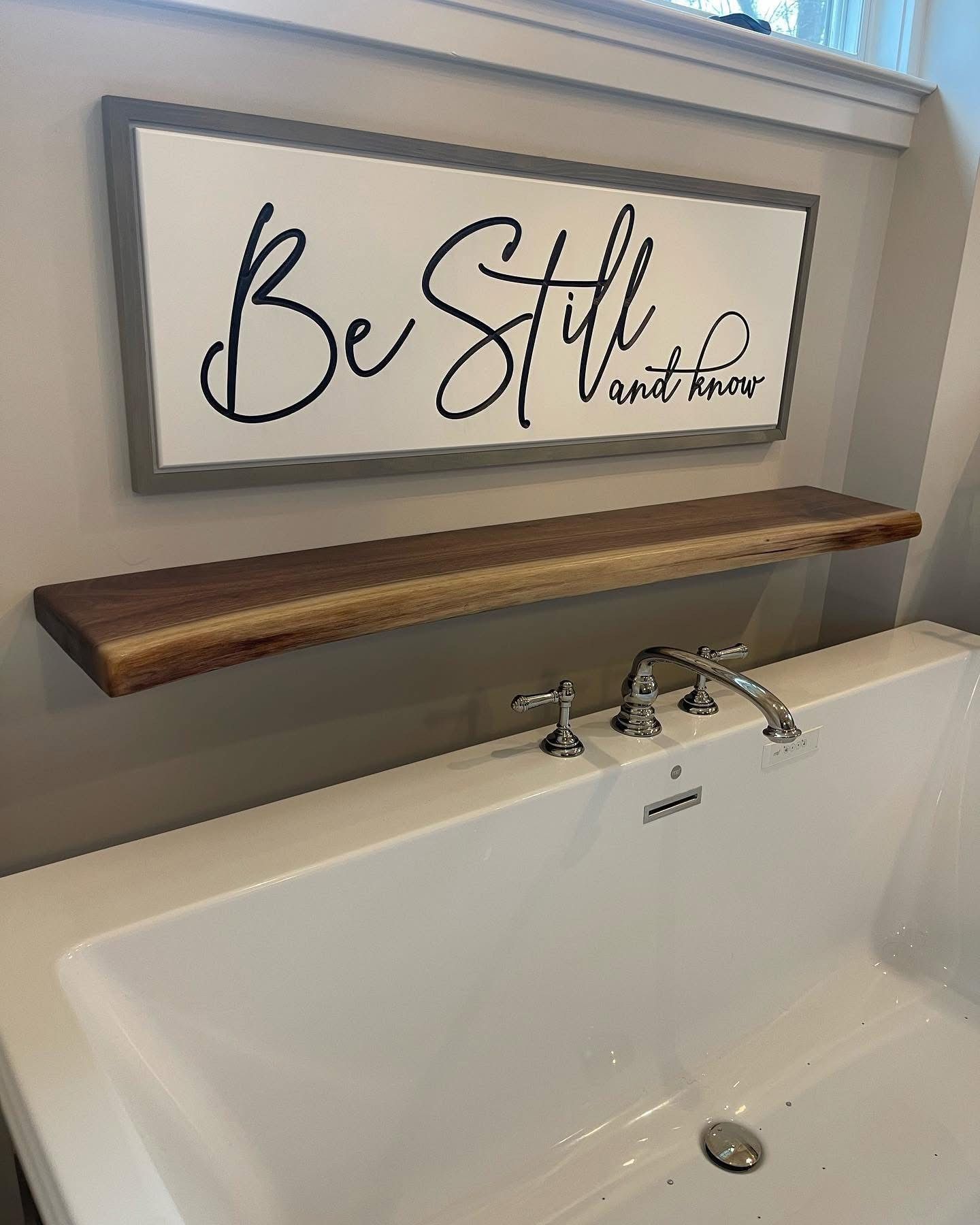 A bathtub with a wooden shelf above it and a sign that says `` be still ''.