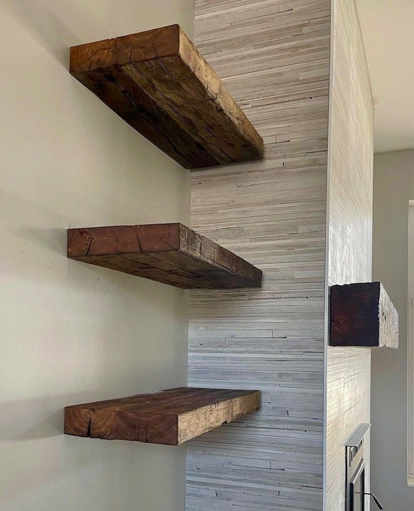 Three wooden shelves are hanging on a wall next to a fireplace.