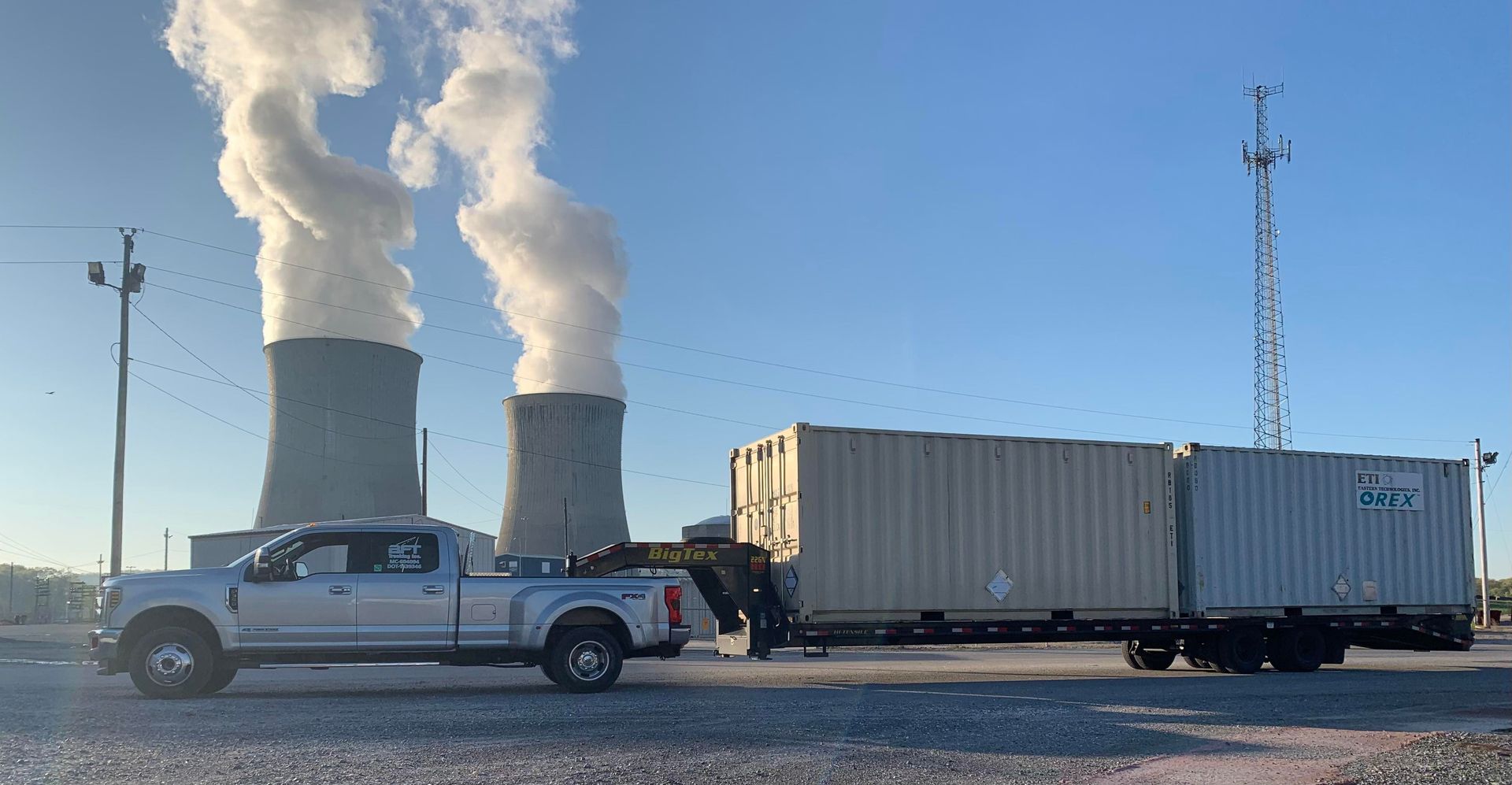 White Ram truck towing a black trailer on a highway, trees in the background.