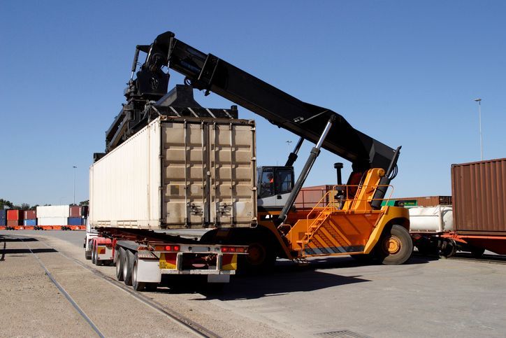 Yellow container handler loading shipping container onto a truck trailer at a port.