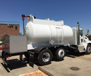 Blue cargo ship in water, moving toward a port with cranes and containers.