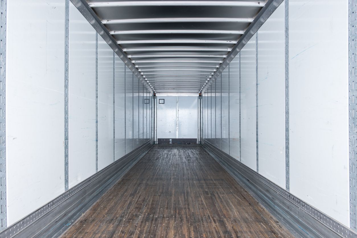 Empty cargo trailer interior, dark wood floor, white walls, and silver ceiling.