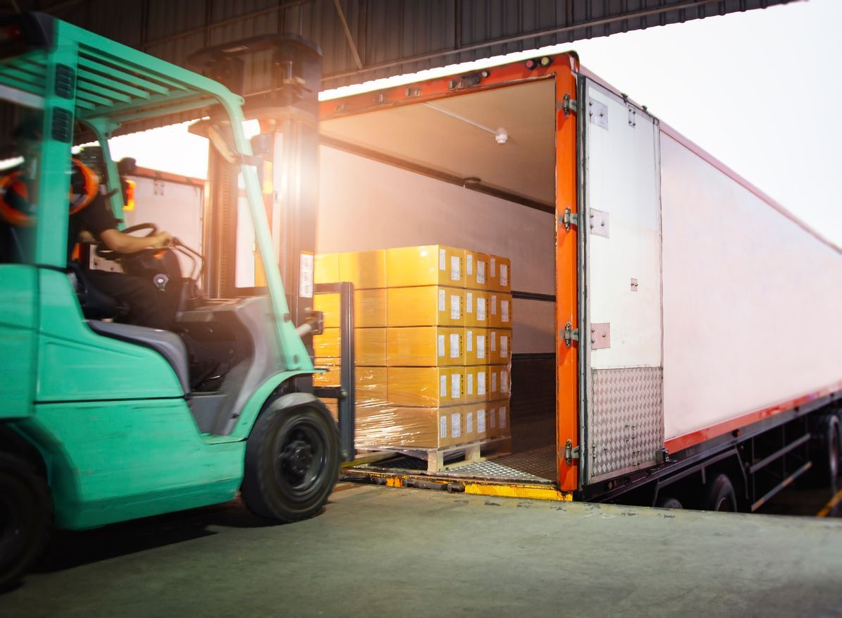 Forklift loading boxes into a semi-truck at a loading dock.