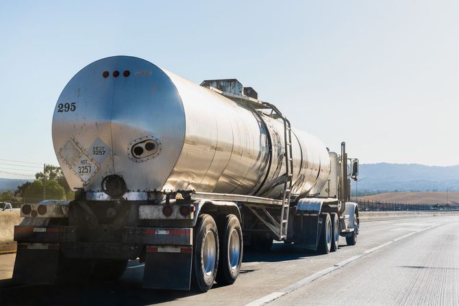 Silver tanker truck driving on a paved road under a clear sky.