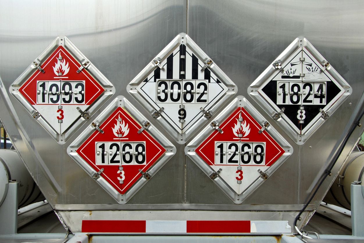 Diamond-shaped hazard warning signs on a metal tank. Various numbers indicate the type of hazardous materials.