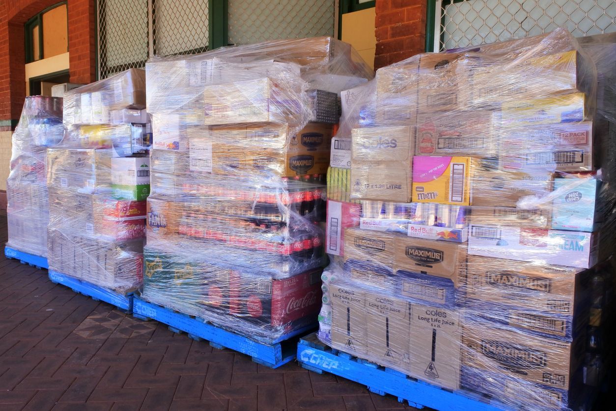 Pallets of packaged food items wrapped in plastic, stacked outside near a building.