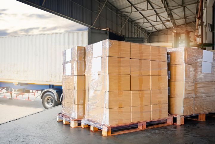 Boxes stacked on pallets near a truck at a loading dock.