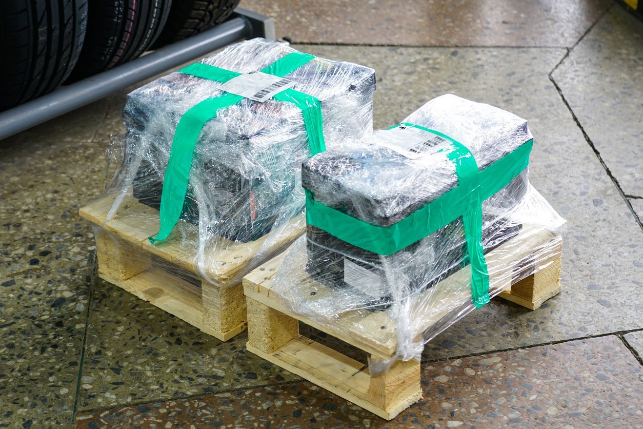 Two car batteries wrapped in plastic and secured with green straps on wooden pallets.