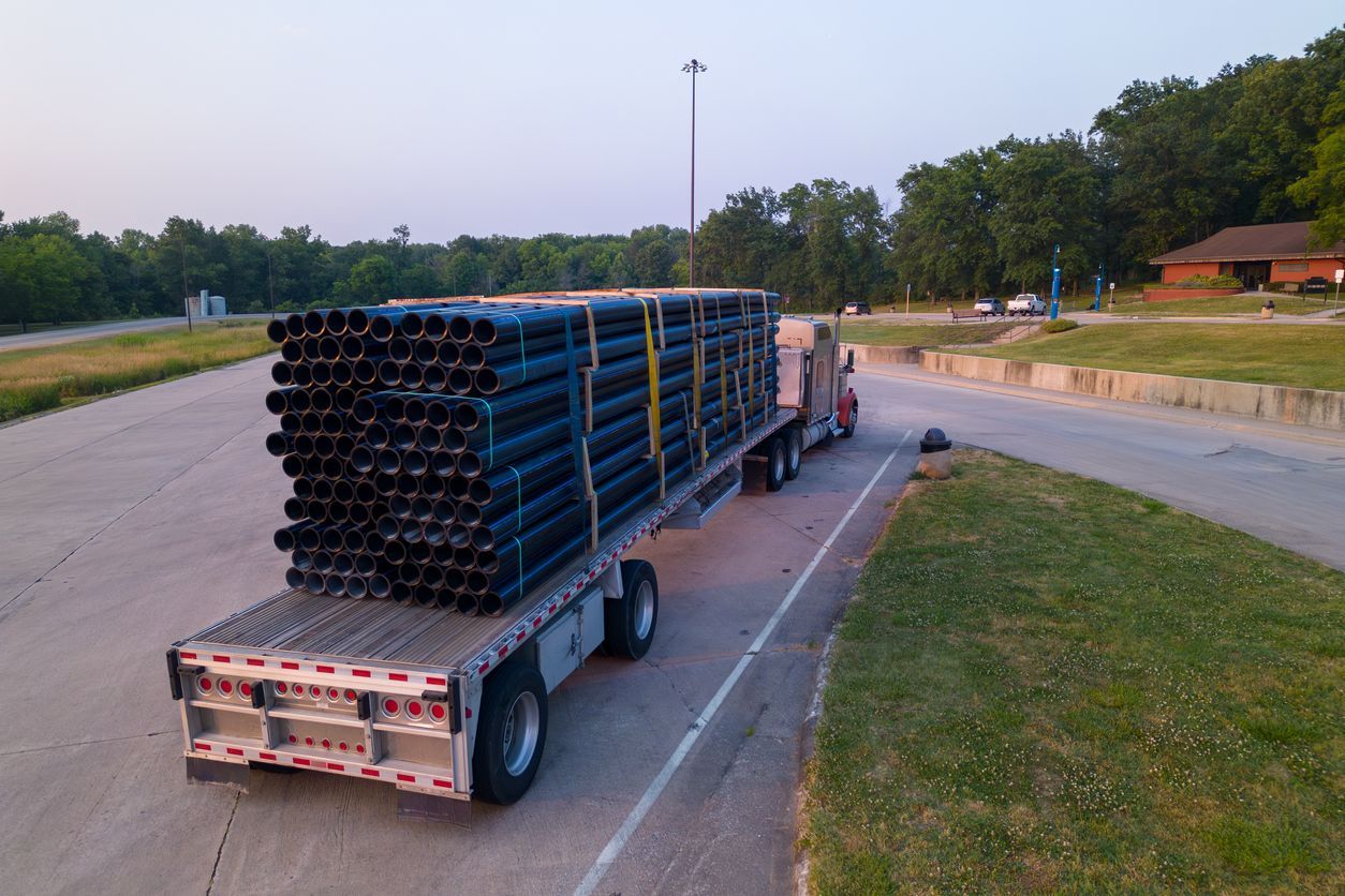 Semi-truck carrying a large load of black pipes on a flatbed trailer, parked on a road.