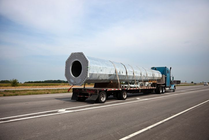 Large metal structure on a flatbed truck traveling on a highway under a blue sky.