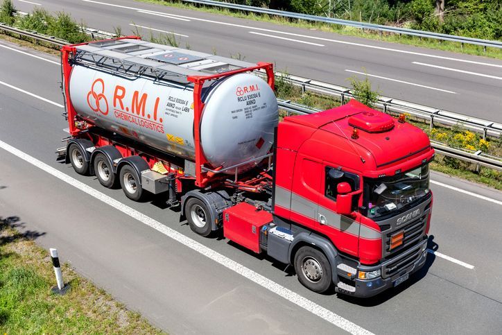 Red semi-truck with a silver tank trailer driving on a highway.