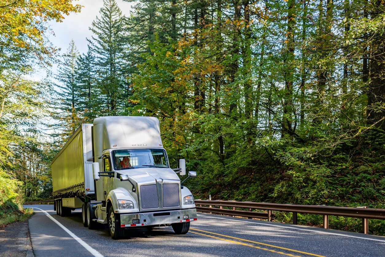 White semi-truck drives on a paved road lined with trees.