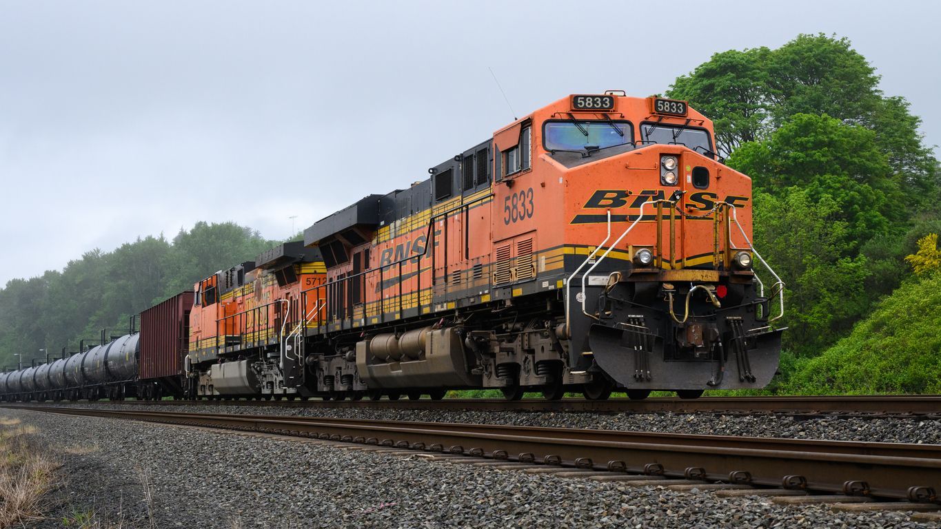 Orange BNSF train with black and yellow detailing travels on tracks alongside trees and gravel.